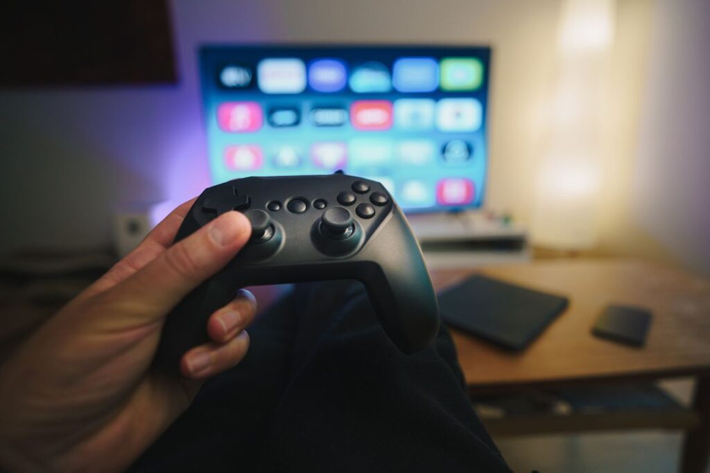 Hænder holder en spillecontroller foran et tv med spilmenu