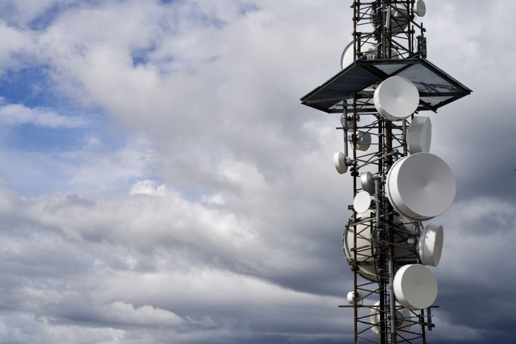 Mobilmast med antenner set nedefra mod en skyet himmel