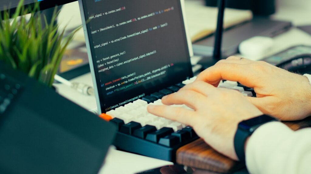 Person skriver på en bærbar computer med kode og terminal på skærmen