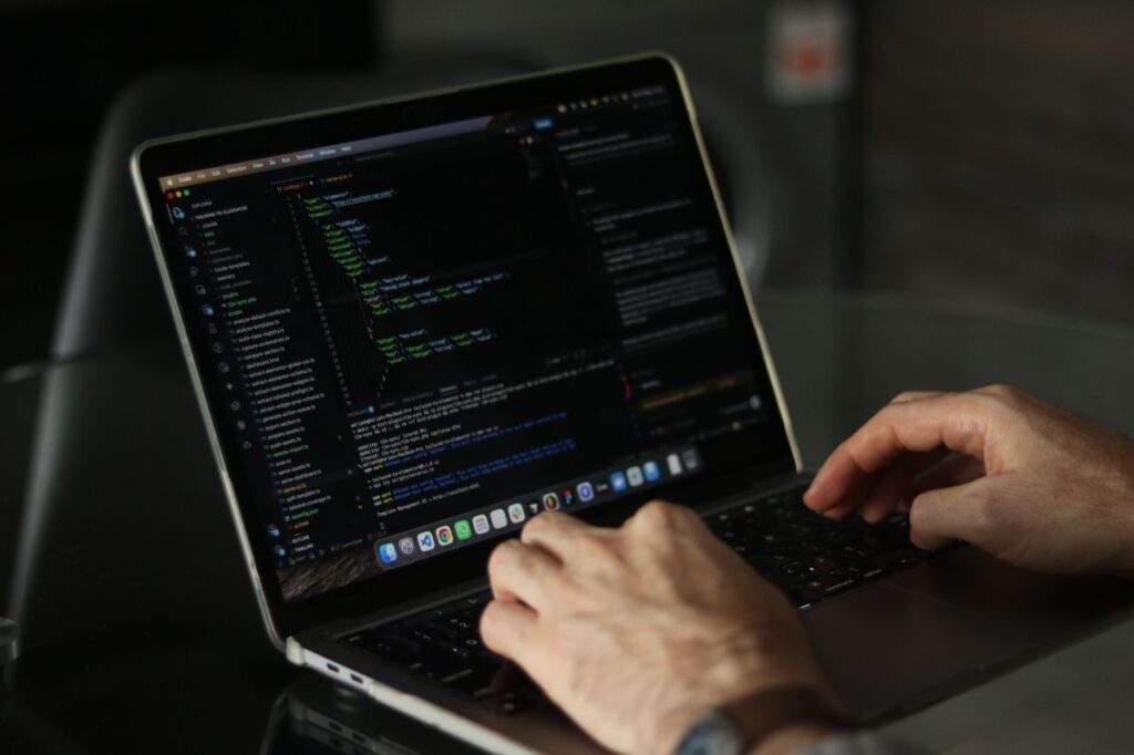 Hænder skriver kode på en bærbar computer i et mørkt rum