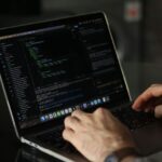 Hænder skriver kode på en bærbar computer i et mørkt rum